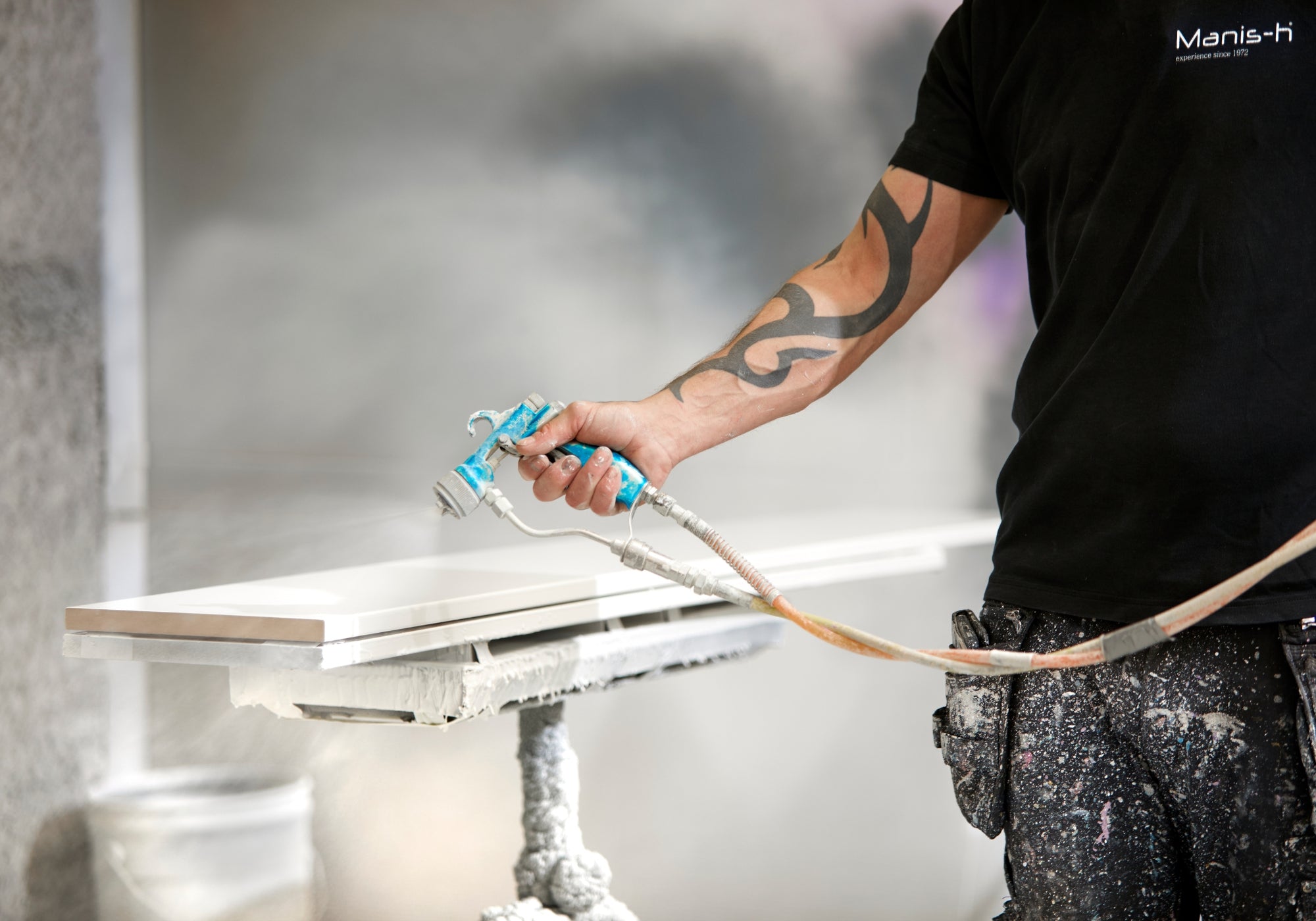 Man med tatovering maler en plade med sprøjtepistol i Manis-h fabrikken