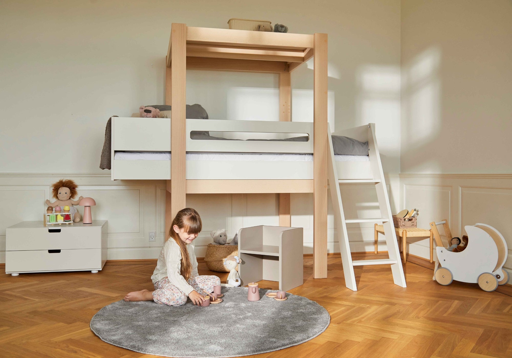 Pige leger på tæppe foran træ køjeseng med stige i børneværelse