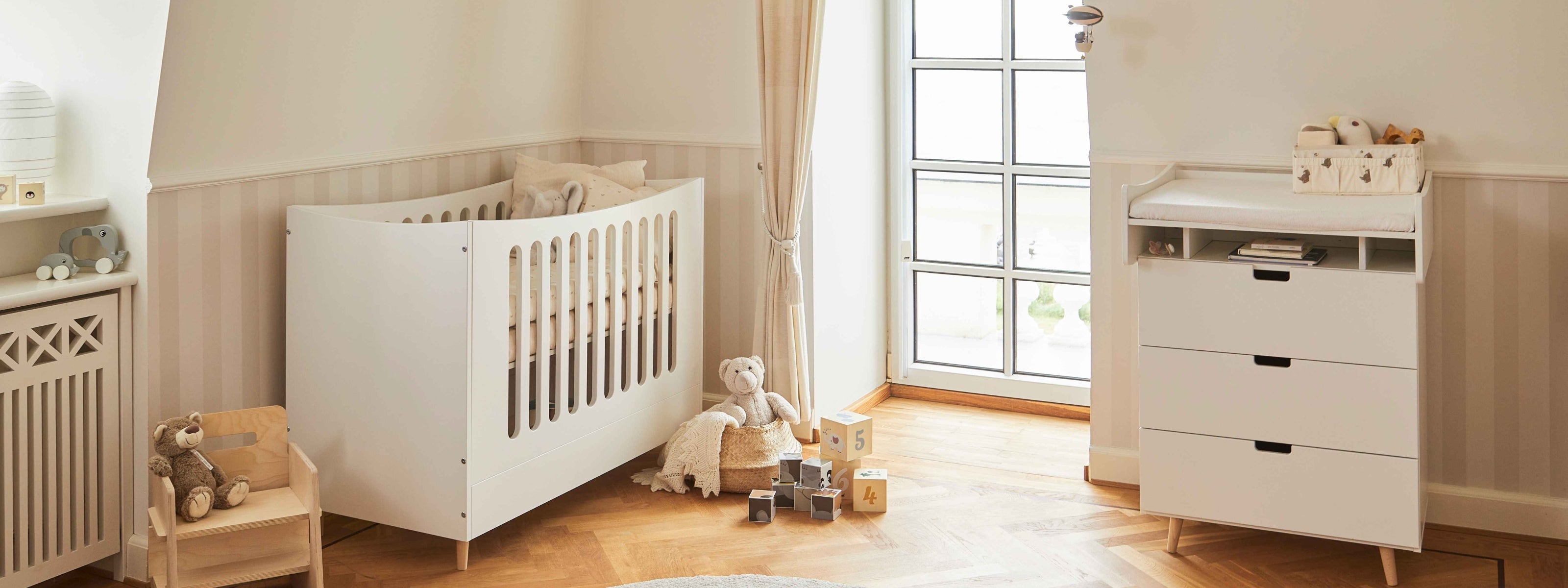 Babyseng og puslekommode i lyst børneværelse med trægulv