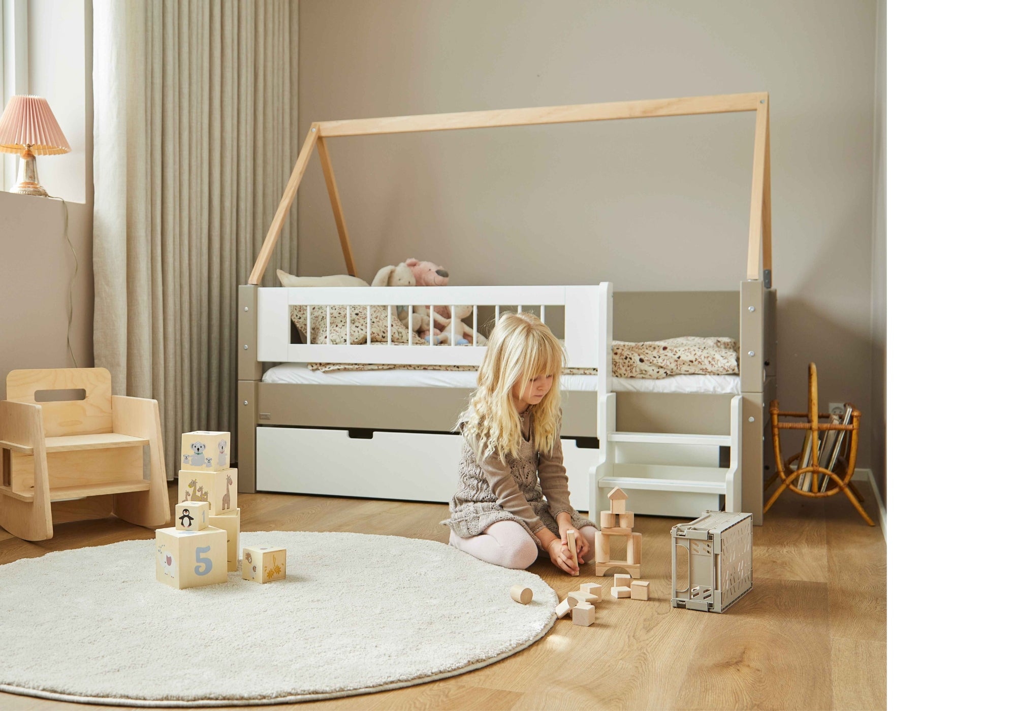 Blond pige leger med klodser foran beige seng med opbevaring