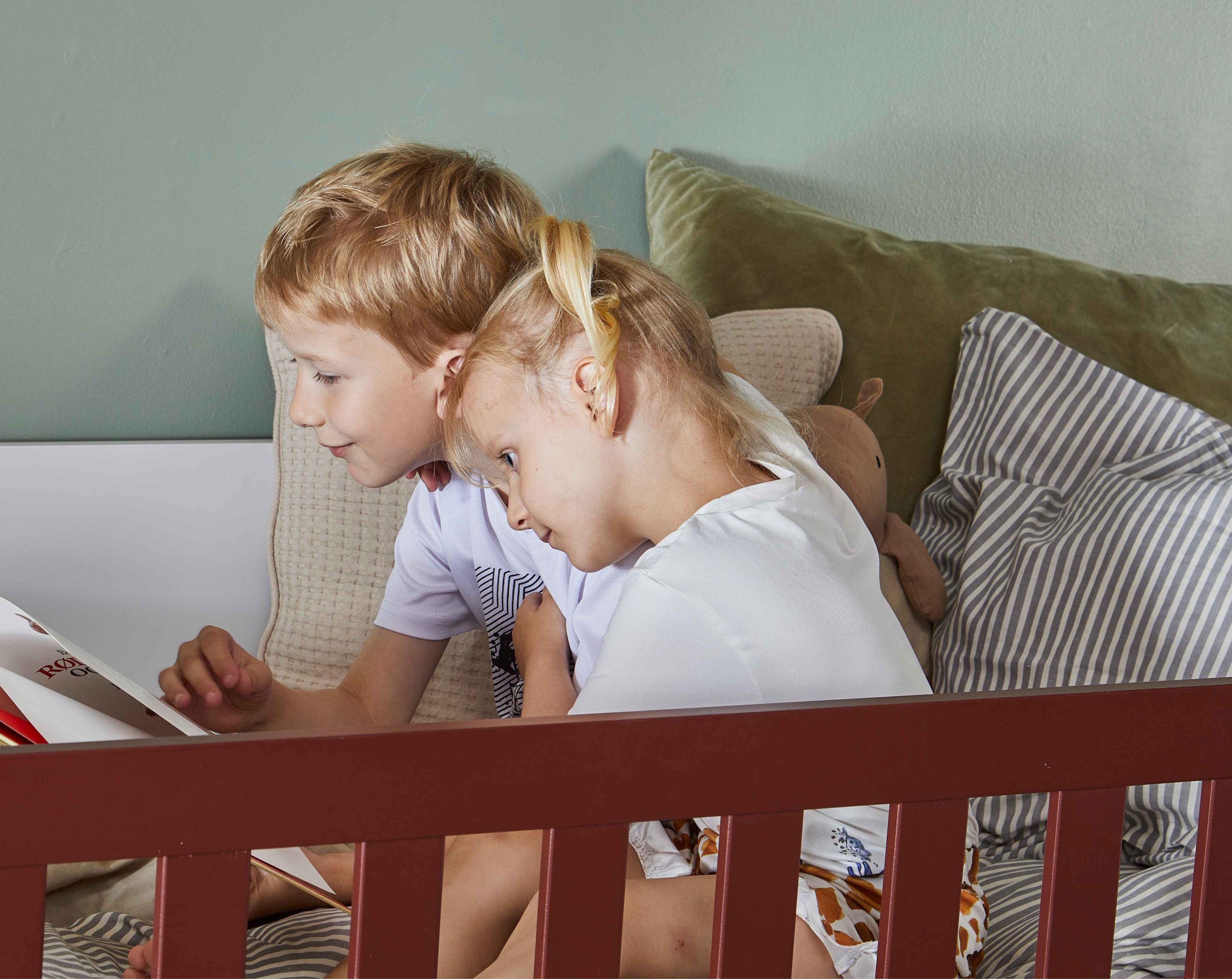 Børn læser bog i rød Manis-h seng med grøn pude og stribet dyne