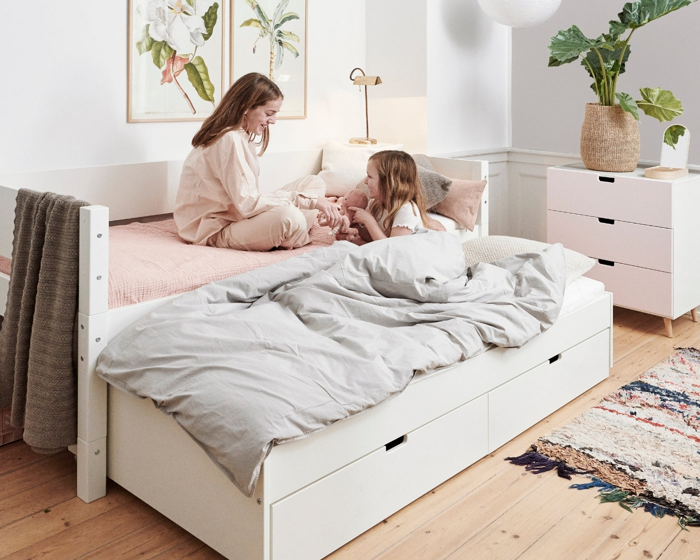 To piger på hvid Manis-h seng med Stars & Flags puder i et børneværelse.