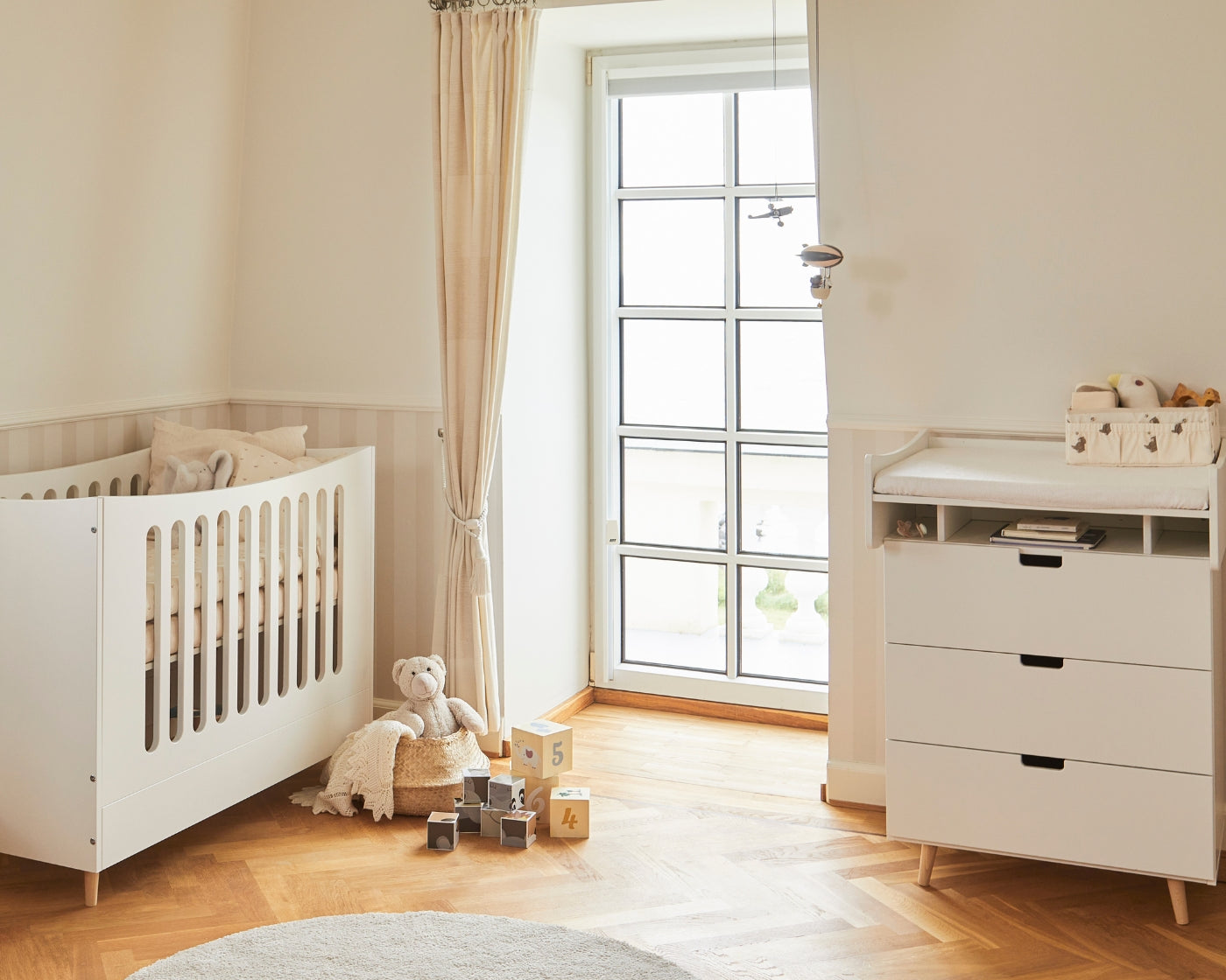 Hvid tremmeseng og matchende puslebord i et lyst børneværelse