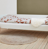 Huxie vit Afros säng med lamellbotten, bruna sängkläder och rund matta